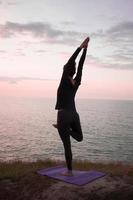 Mujer en forma haciendo ejercicio de estiramiento de yoga al aire libre en un hermoso paisaje montañoso. hembra en la roca con asanes de entrenamiento de fondo de mar y amanecer o atardecer. silueta de mujer en posturas de yoga foto