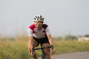 corredor de bicicletas en entrenamiento de casco y ropa deportiva solo en caminos vacíos, campos y fondo de árboles foto