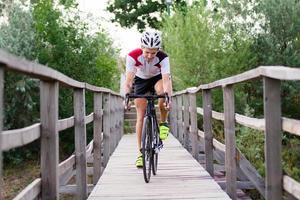 ciclista profesional en uniforme y casco en el viejo puente de madera, fondo del campo foto