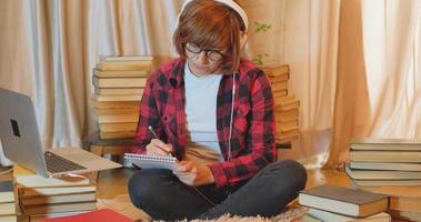 Young woman student studying at home with many books and laptop video
