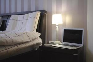 laptop in bedroom with bed, lamp and home decor background. photo