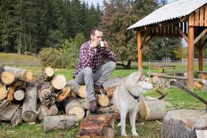 turista relajándose en la madera cortada con un perro husky y bebiendo té o café foto