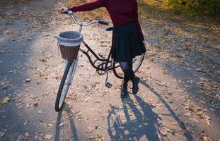 mujer joven en el parque de otoño lee un libro, hermosa mujer pelirroja con bicicleta en la hierba verde foto