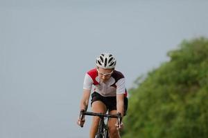 Bicycle racer in helmet and sportswear training alone on empty country road, fields and trees background photo
