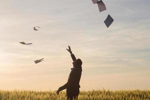 Portrait of young businessman throwing sheets of paper into the air, sunset in summer fields background photo