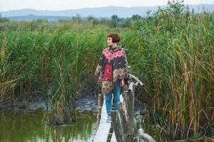 una joven viajera vestida con un poncho camina al aire libre en los campos de otoño foto