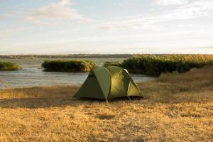 Green tent of hikers near river during the sunset or sunrise photo