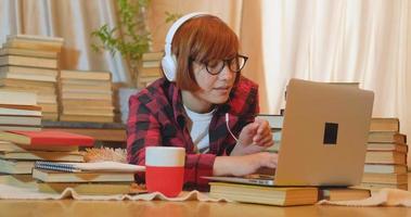 Young woman student studying at home with many books and laptop video