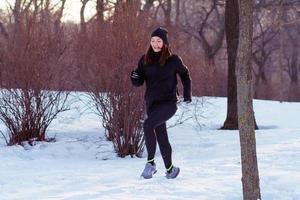 young woman athlete in black sport suit run in winter park photo