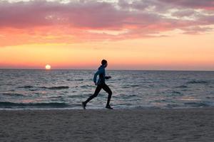 joven con ropa de otoño entrenando en la playa, fondo de amanecer, corredor masculino por la mañana foto