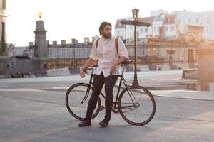 joven barbudo con mochila de cuero caminando con bicicleta negra foto