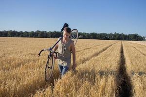 un joven monta una bicicleta de piñón fijo en la carretera rural, los campos y el fondo del cielo azul foto