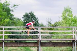 ciclista profesional en uniforme y casco en el viejo puente de madera, fondo del campo foto