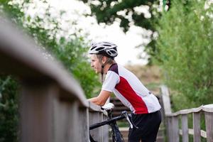 Professional bicucle rider in uniform and helmet on the old wooden bridge, country side background photo