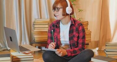 Young woman student studying at home with many books and laptop video