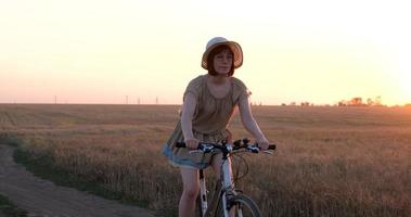 giovane donna con cappello giro in bicicletta nei campi di grano estivi video