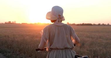 jeune femme avec chapeau balade à vélo dans les champs de blé d'été video