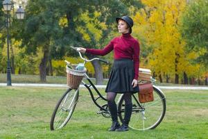 mujer joven en el parque de otoño lee un libro, hermosa mujer pelirroja con bicicleta en la hierba verde foto