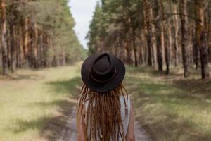 young woman with dreadlocks walking on the road, big pines background, girl hiker in woods photo