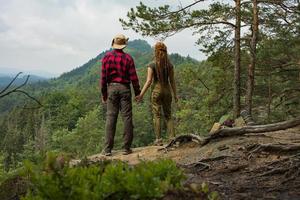 Couple of travelers standing on the cliff and watching beautiful mountains and forest photo