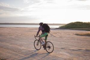 turista en bicicleta con mochilas y casco viaja en el desierto en su bicicleta de ciclocross durante la puesta de sol foto