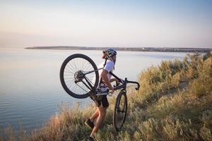 Bicycle rider on professional cyclocross bike ride downhill, pine and lake background photo