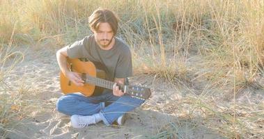 joven y apuesto hombre tocando guitarra acústica en la playa en un día soleado, mar u océano en el fondo foto