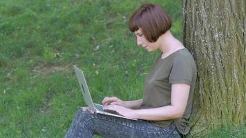 jovem trabalha com laptop ao ar livre no parque de verão, fêmea com computador na grama verde 4k tiro