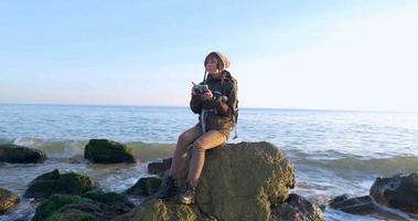 joven viajera con mochila y cámara de cine retro viaja en las montañas de otoño cerca del mar video