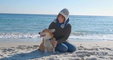 jonge vrouw speelt met corgi-hond op het zeestrand