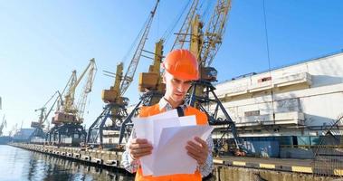 male worker of sea harbor in orange helmet and safety west, cranes and sea background photo