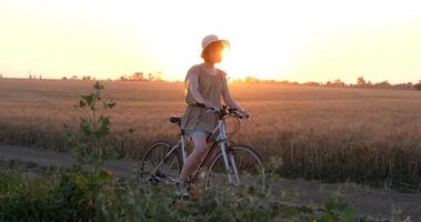 jeune femme avec chapeau balade à vélo dans les champs de blé d'été video