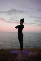 Fit woman doing yoga stretching exercise outdoor in beautiful mountains landscape. Female on the rock with sea and sunrise or sunset background training asans. Silhouette of woman in yoga poses photo