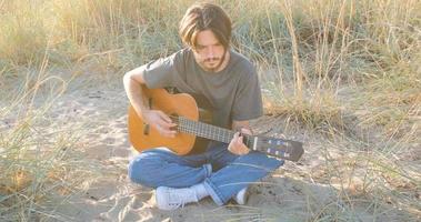 Young handsome male play in acoustic guitar on the beach in sunny day, sea or ocean on background photo