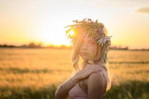 retratos de mujeres jóvenes pasándola bien en el campo de trigo durante la puesta de sol, dama en la corona de flores de la cabeza durante
