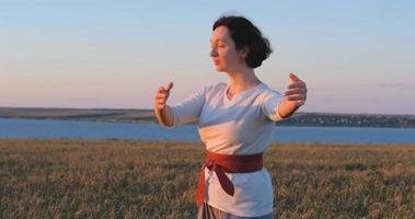 mujer practicando qigong en campos de verano con hermosa puesta de sol en el fondo foto