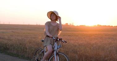 jovem mulher com chapéu andar de bicicleta em campos de trigo de verão video