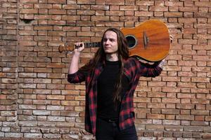 Young male with long hair and tattoo play on acoustic guitar outdoors on the street photo