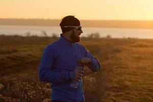 young man trail runner training outdoors in the fields, sunset in lake background photo