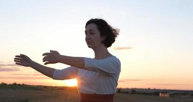 Female practicing qigong in summer fields with beautiful sunset on background