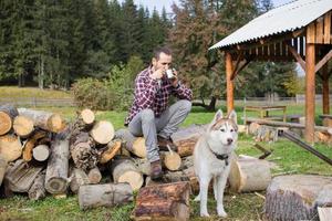 turista relajándose en la madera cortada con un perro husky y bebiendo té o café foto