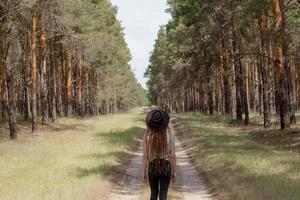 young woman with dreadlocks walking on the road, big pines background, girl hiker in woods photo