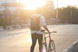 joven barbudo con mochila de cuero caminando con bicicleta negra foto