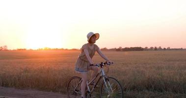 jeune femme avec chapeau balade à vélo dans les champs de blé d'été