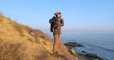 junge weibliche reisende mit rucksack und retro-filmkamera reisen in den herbstbergen nahe meer video