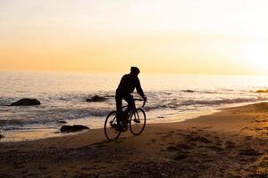 silueta de un joven ciclista con casco en la playa durante la hermosa puesta de sol foto