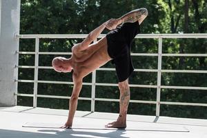 Young male with tattoos do yoga exercises outdoors on balcony photo