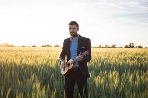 Happy manager with ukulele travel in summer wheat fields, buisinesman in suit play on ukulele, vacation or travel concept photo