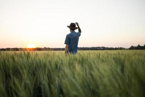 joven agricultor independiente en el campo de trigo durante la puesta de sol foto