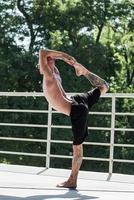 Young male with tattoos do yoga exercises outdoors on balcony photo